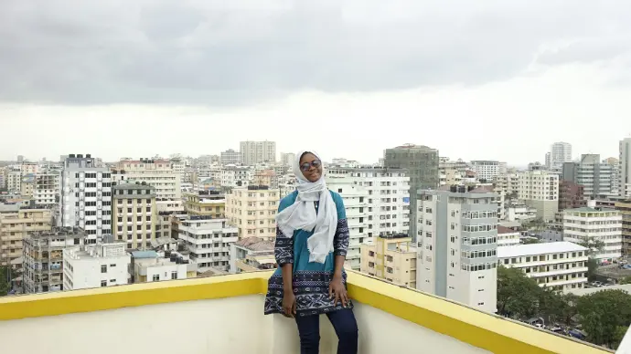 woman in white long sleeve shirt and blue denim jeans standing on yellow concrete wall during